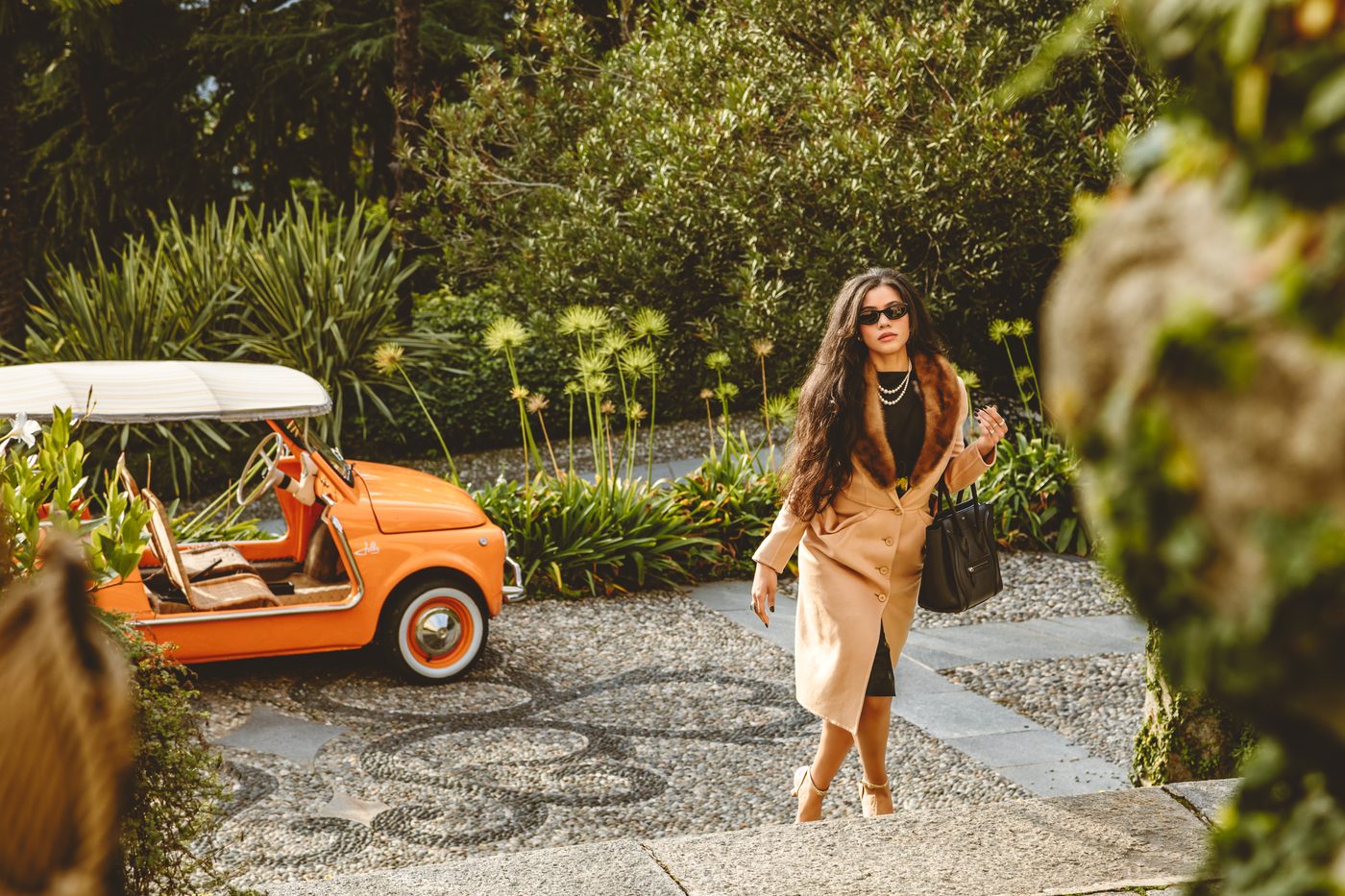 Simone in a camel coat beside an orange Fiat